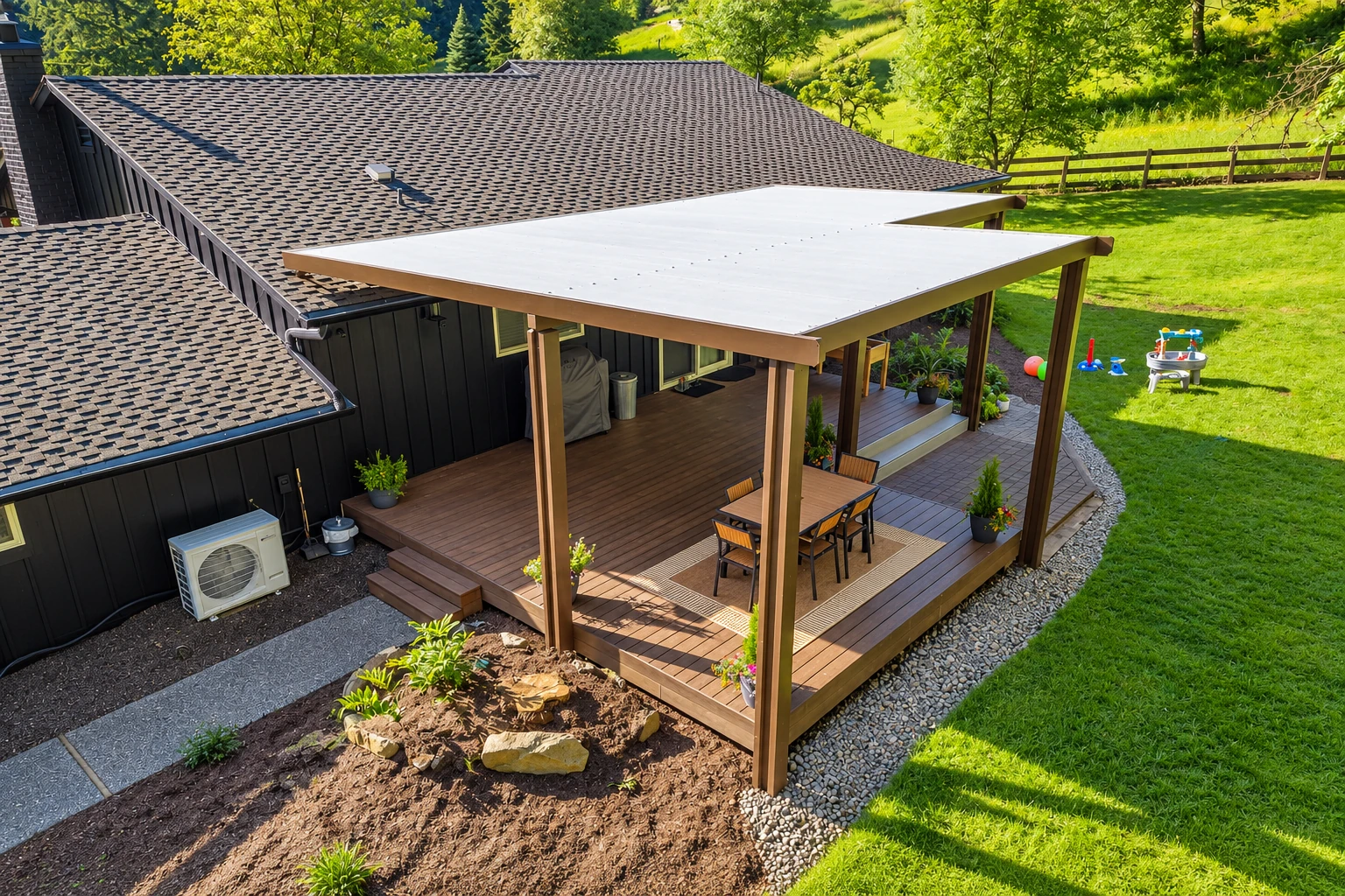 A broad white patio cover shades a wood deck with a dining table beside a dark-sided house and green lawn.