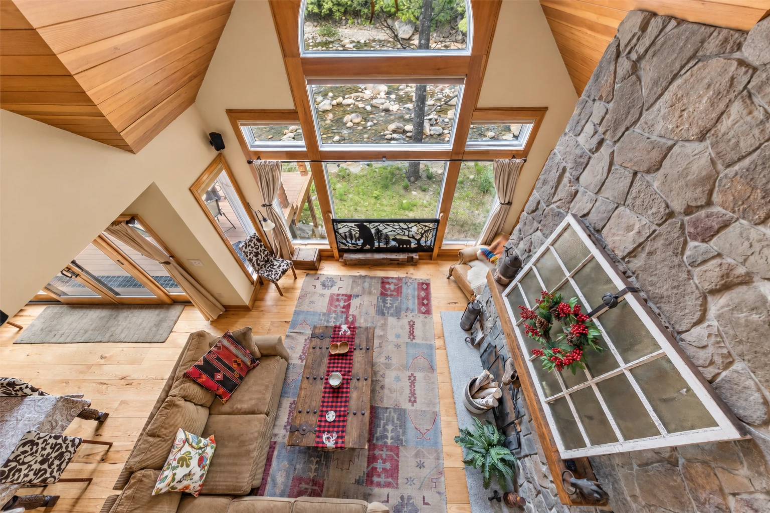 Overhead view of a vaulted sunroom with expansive windows, wood floors, a stone wall, and seating.